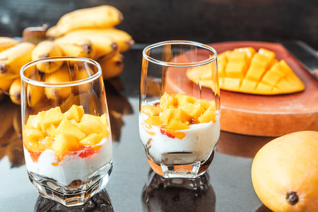 Glasses of yoghurt with mango and strawberry. Homemade healthy yogurt with fruits. A banch of bananas on a tableの写真素材