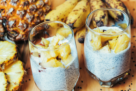 Glass of chia seeds pudding with mango. Basil seeds in coconut milk with sliced ??pineapple and banana on a wooden table. A banch of bananasの写真素材