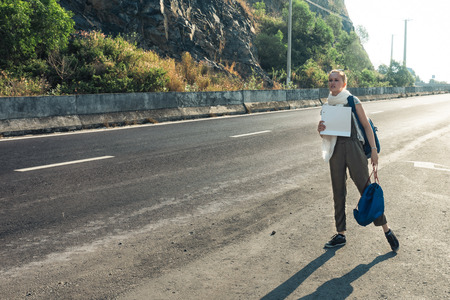 Tired girl with blue backpack holding a white blank cardboard sign. Hitchhiking at sunset or sunrise