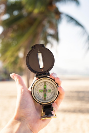 Woman hand holding a compass on the beach. Sand and blue sea, sky. Vertical viewの写真素材