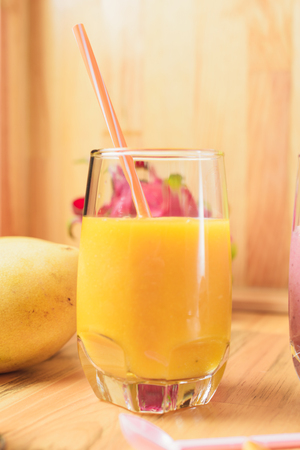 Mango shake with drinking straw and spoon on light wooden table. Dragon fruit, passion fruit on backgroundの写真素材