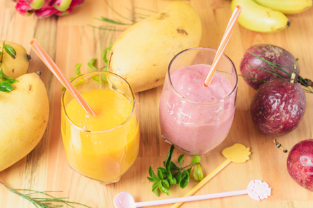 Mango shake with drinking straw and spoon on light wooden table. Dragon fruit, passion fruit on backgroundの写真素材
