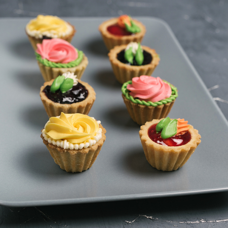 Row of colorful cupcakes on a gray plate. Cakes with cream and jam on a stone backgroundの写真素材