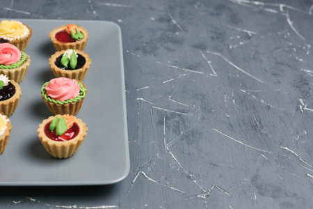 Row of colorful cupcakes on a gray plate. Cakes with cream and jam on a stone backgroundの写真素材