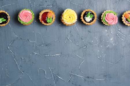 Row of colorful cupcakes on a gray table. Cakes with cream and jam on a stone backgroundの写真素材
