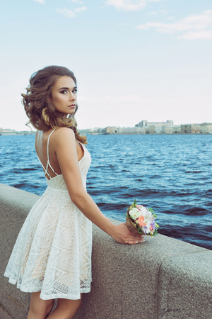 Pretty young woman waiting on Promenade. Pretty young woman waiting on Promenade. Beautiful girl in white summer dress. Whiting for a groomの写真素材