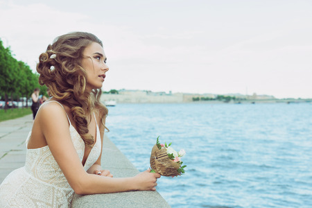 Pretty young woman waiting on Promenade. Beautiful girl in white summer dress. Whiting for a groomの写真素材