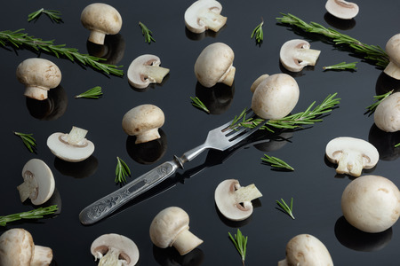 Common mushroom on a vintage fork. Sliced ??champignon and rosemary on the stainless steel fork isolated on a black backgroundの写真素材