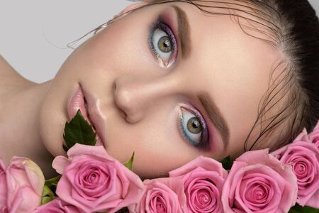 Studio portrait of a beautiful young woman. Fashionable brunette model with sexy pink lips and perfect makeup lying on rosesの写真素材