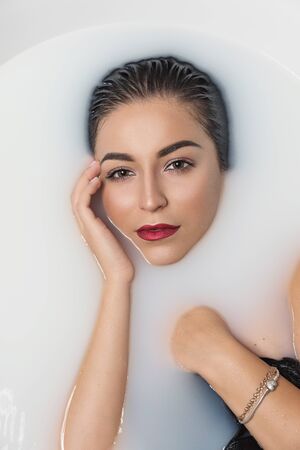 Fashion model girl taking milk bath. Beauty young woman with bright makeup relaxing in bath, spa and...