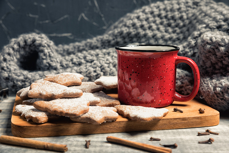Red cup and gingerbread cookies. Fresh baked star and fir-tree shaped biscuits on a wooden background. Gray plaid or scarfの写真素材