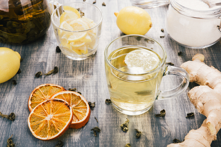 Glass mug of green camomile hot tea on wooden table. Sliced lemons on a chopping boardの写真素材