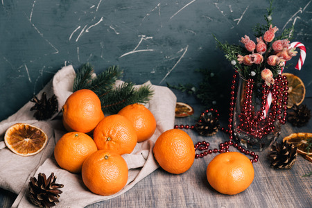 Sweet fresh tangerine on the wooden table. Christmas composition with fir tree brunches, pine cones, berries, candys and dry oranges.の写真素材