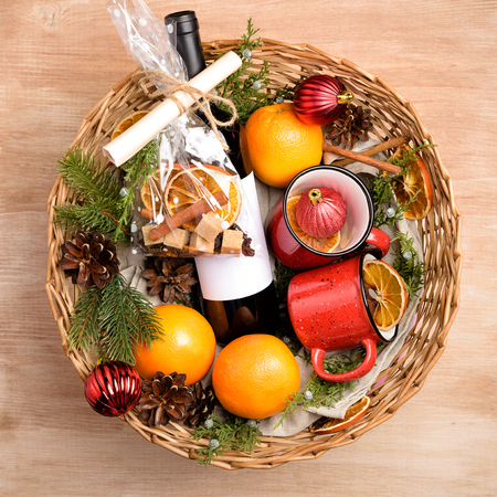 Bottle of red wine in gift basket. Mulled wine with oranges, cups and fir-tree ornaments in the present box. Top viewの写真素材
