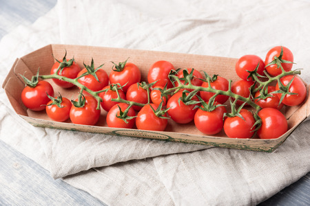 Small red cherry tomatoes in box. Fresh farmer vegetables in basket on an old wooden table in a rustic style, selective focusの写真素材
