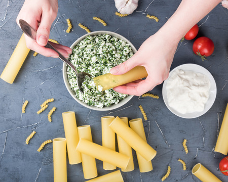 Female hands holding raw cannelloni. Woman cooking traditional italian food. Tomatos, pasta, sauce. Spinach and ricotta in bowlの写真素材
