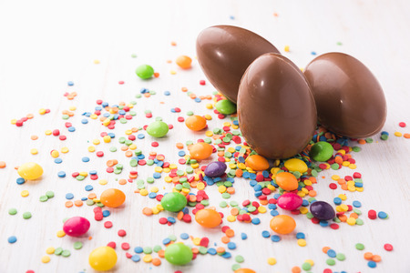 Easter chocolate egg with colorful candies. Sweet eggs on a white wooden backgroundの写真素材