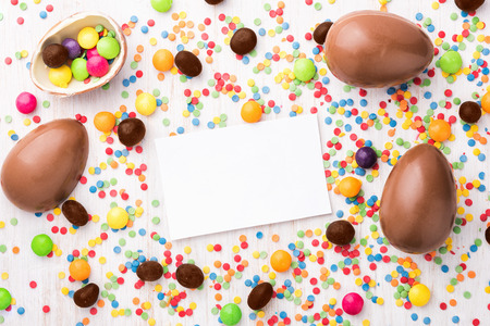 Easter chocolate egg with colorful candies. Sweet eggs on a white wooden background. Paper noteの写真素材