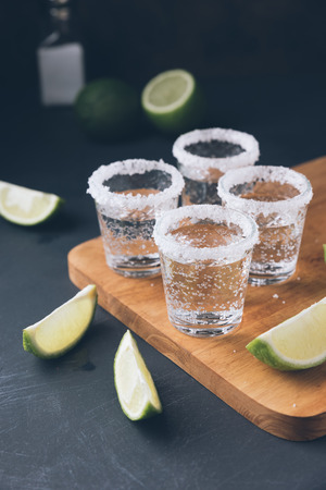 Alcohol shots on wooden tray. Shooter glasses of vodka or Tequila whit salt on black tableの写真素材