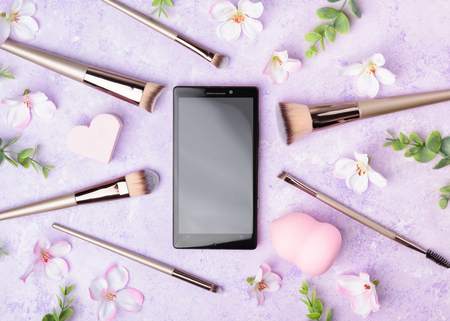 Set of makeup brushes on pink background. Cosmetic, beauty blender and a beautiful spring flowers. Online shopping concept. Top view, flat lay.の写真素材