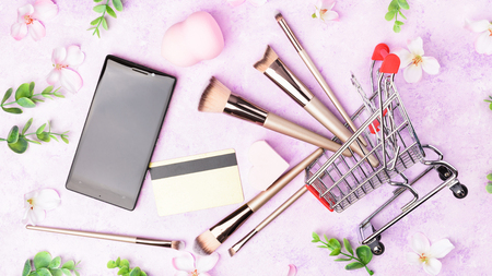 Set of makeup brushes on pink background. Cosmetic, beauty blender and a beautiful spring flowers. Online shopping concept. Top view, flat lay.の写真素材