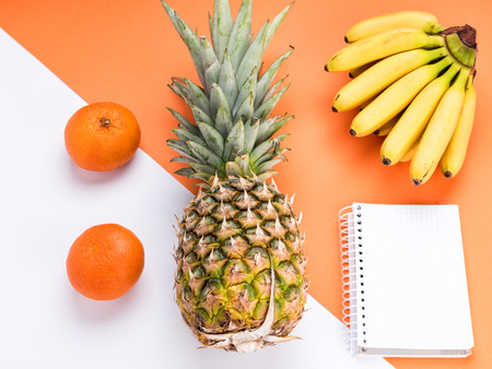Notebook and Tropical Fruits on an orange and white background. Creative concept, flat layの写真素材
