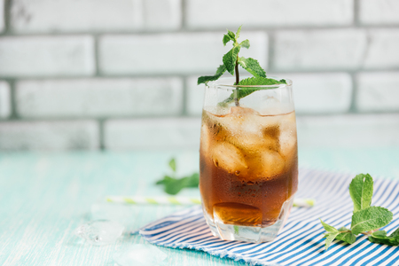The glass of peach ice tea on wooden table. Cuba Libre or long island iced tea cocktail, cold drink or lemonade with fruits and mintの写真素材