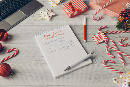 Writing New Year's resolutions and goals with a red marker in the notebook. Laptop with Christmas...