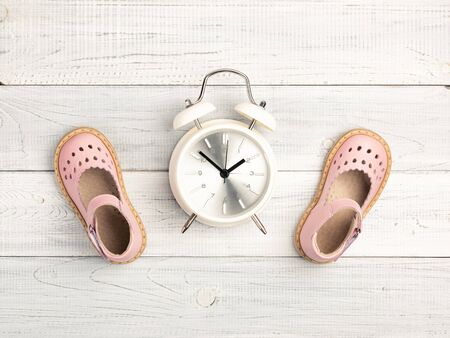 Summer Pink Baby girl shoes and white alarm clock on wooden background. Top view trendy leather sandal, flat lay. Copy space for your textの写真素材