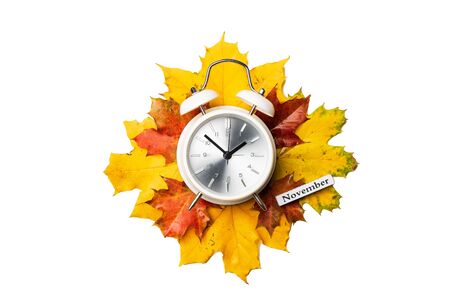 Alarm clock on yellow and red foliage isolated on white background. Time change concept, october