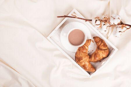 Morning breakfast on a wooden tray with a cup of coffee or cocoa croissant in bed. Hotel Room concept, copy space. Top view, flat layの写真素材