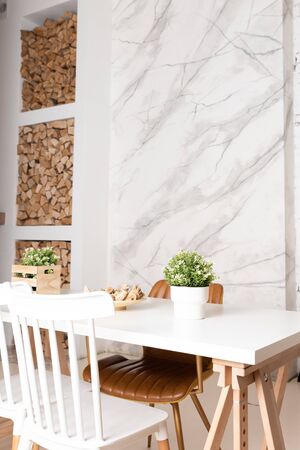 Bright dining room with big white wooden table. Marble wall on the background, firewood for a fireplaceの写真素材