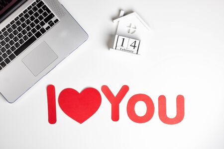 Valentine's Day composition on white table. Female desktop laptop keyboard, notebook, lollipop love, and red heart shape pen. Flat lay, top view, copy spaceの写真素材