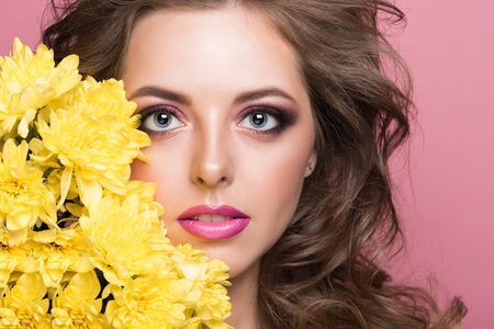 Pretty woman with makeup and hairstyle like in the 80s. Beauty female face with perfect skin on a pink background and yellow flowersの写真素材