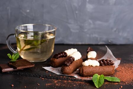 Chocolate rum balls with green mint tea on dark background. Brown sweets with cream