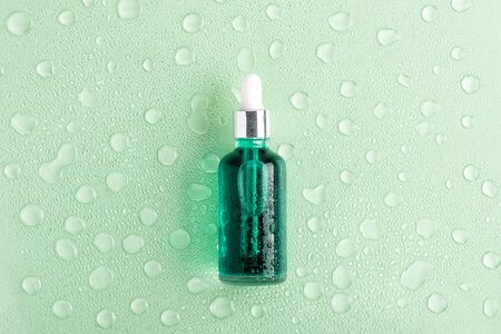 Moisturizing beauty essence in a dropper glass bottle on green background with water drops. Spa bathroom concept, copy space for your textの写真素材