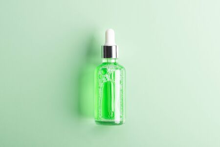 Moisturizing beauty essence in a dropper glass bottle on green background. Spa bathroom concept,...