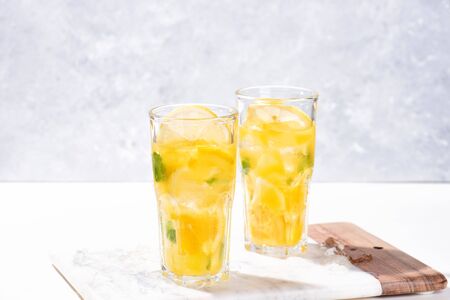 Citrus lemonade or mojito cocktail with lemon and orange and basil. Cold beverage or drink with ice on marble cutting boardの写真素材