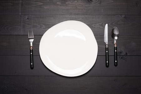 Table setting with empty white plate. Tableware on dark wooden backgroundの写真素材