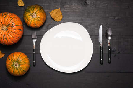 Autumn table setting with empty white plate and pumpkins. Halloween or thanksgiving tableware on dark wooden backgroundの写真素材