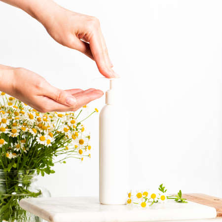 Woman pushing pump plastic lotion or soap bottle with copy space. Young female hands, and chamomile...