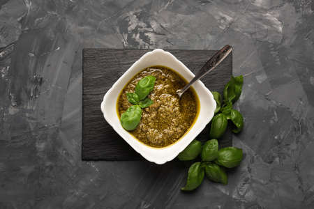 Bowl with pesto and fresh basil, garlic, parmesan cheese, pine nuts and olive oil on marble board. Kitchen table with Italian sauceの写真素材