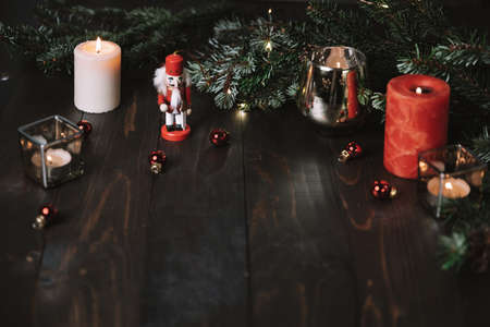 Christmas glowing small candle, nutcracker and fir tree branches on old wooden background, dark...