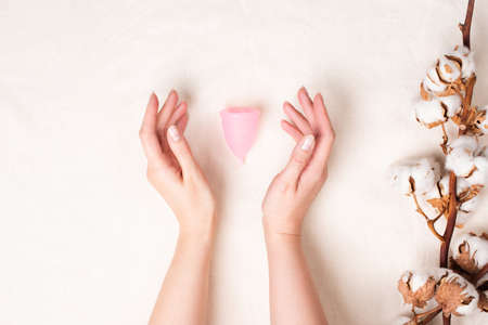 Menstrual cup in woman hands. Feminine hygiene product on cotton fabric beige backgroundの写真素材