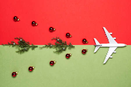 Airplane, ornaments and ornaments and thuja plants on red and green paper background. Christmas or New Year festive concept. Flat lay, top view.の写真素材