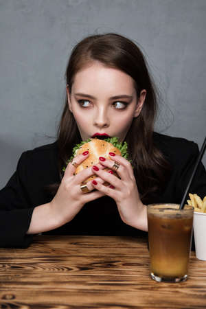 Glamor woman with a perfect fashion red manicure and makeup eating burger and French fries. Fast food conceptの写真素材