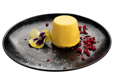Mango cheesecake on black plate garnished with red strawberry sweet powder and flower. Isolated on white backgroundの写真素材