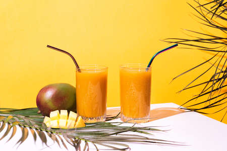 Glass of fresh mango juice cocktail and palm branchesの写真素材