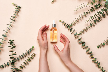 Female hand holds glass bottles of essence or serum with natural eucalyptusの写真素材