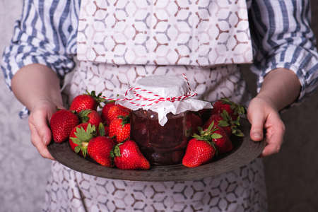 Woman holds a metal copper tray with a jar of strawberry jamの写真素材